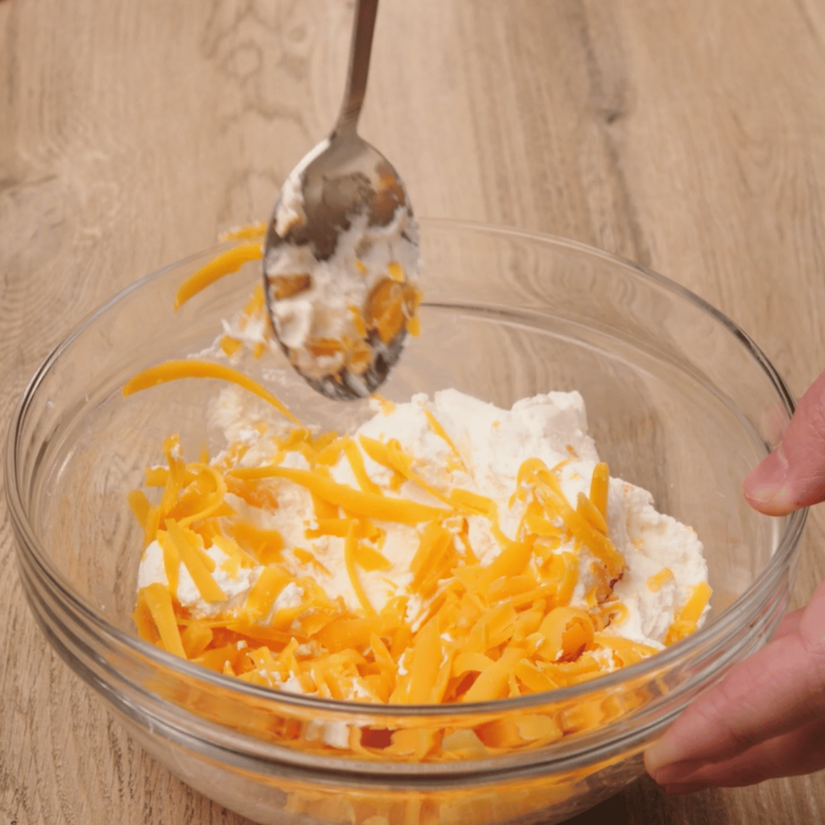 cream cheese and cheddar cheese being combined in a glass bowl for the bacon wrapped jalepeno poppers. 