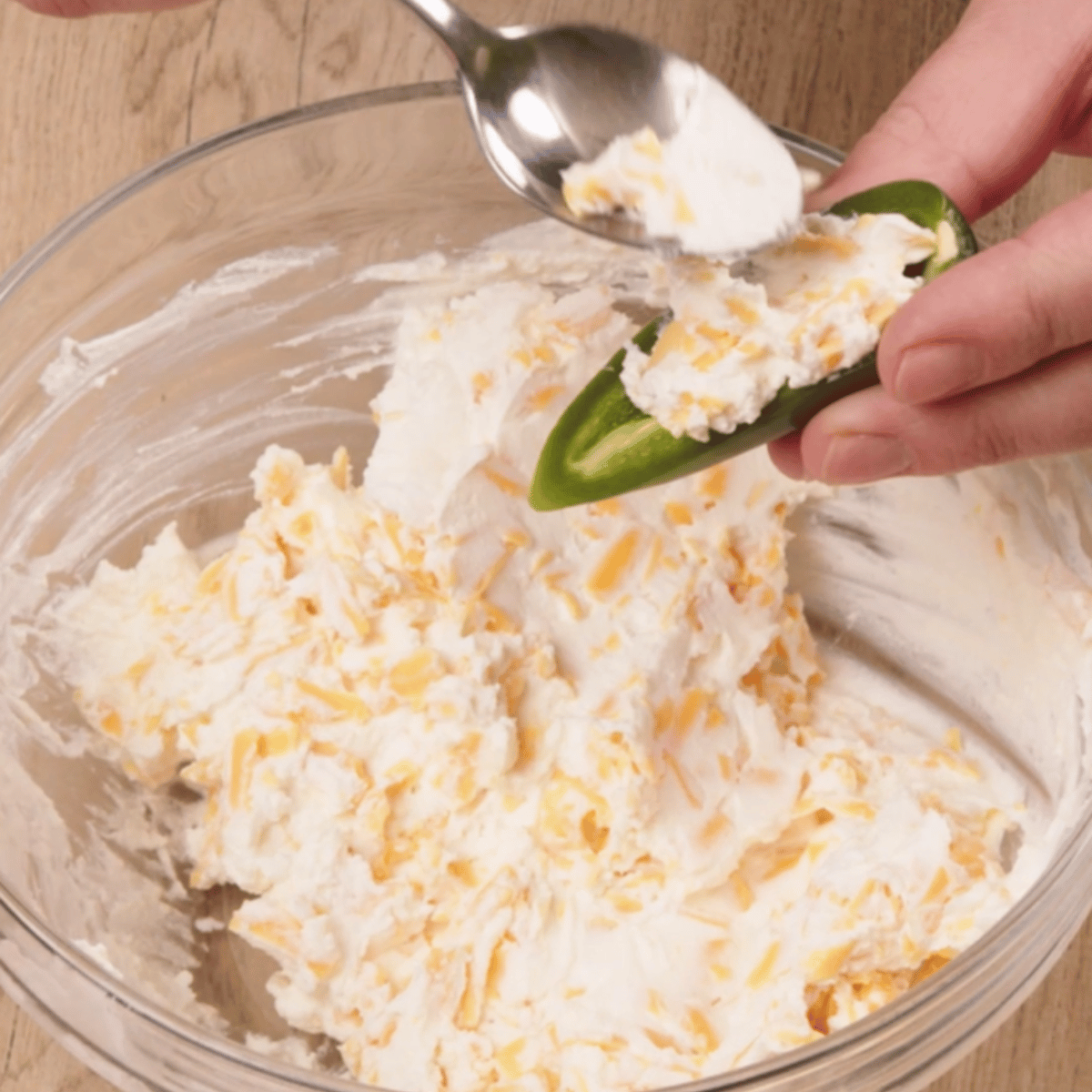 adding cream cheese mixture with a spoon into the halved jalepeno.