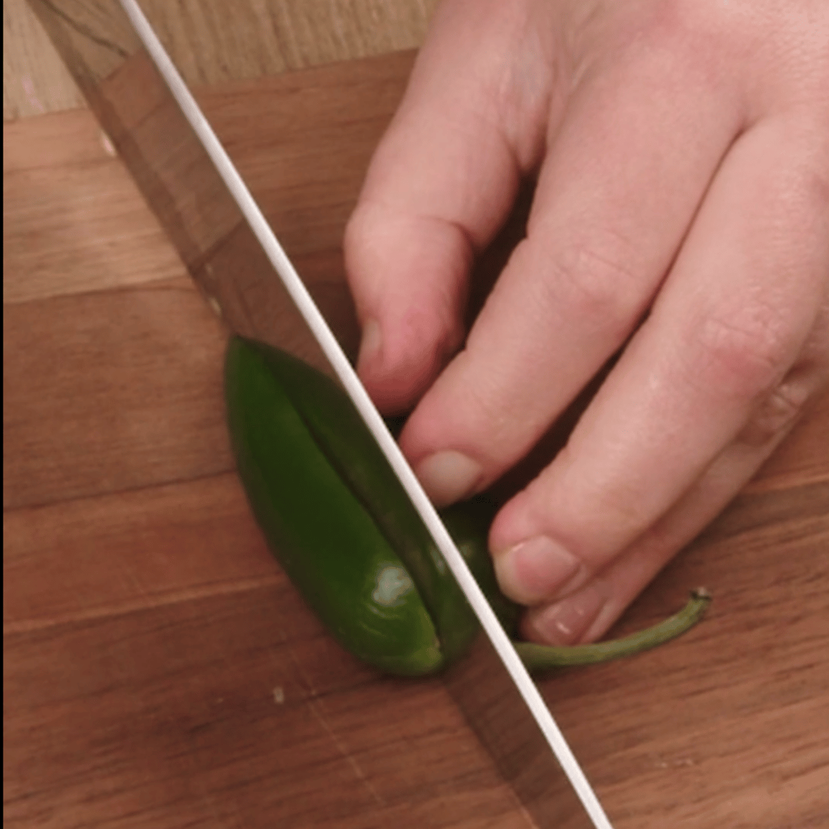 slicing a jalepeno in half with a large knife on a cutting board. 