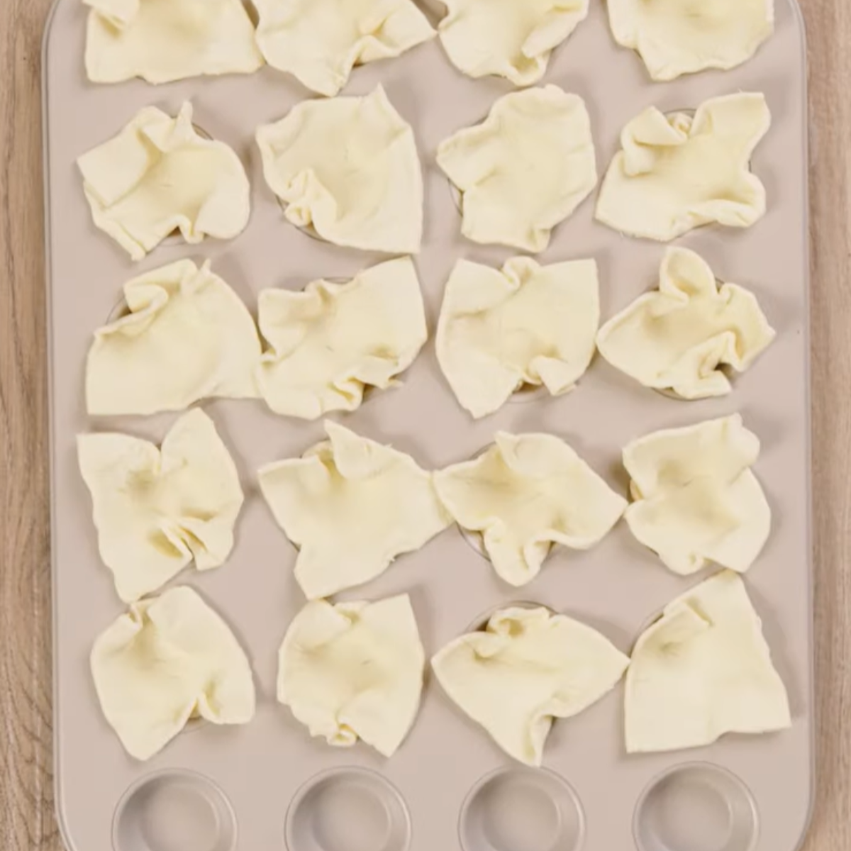 Squares of puff pastry dough pressed into a muffin tin, forming cups.