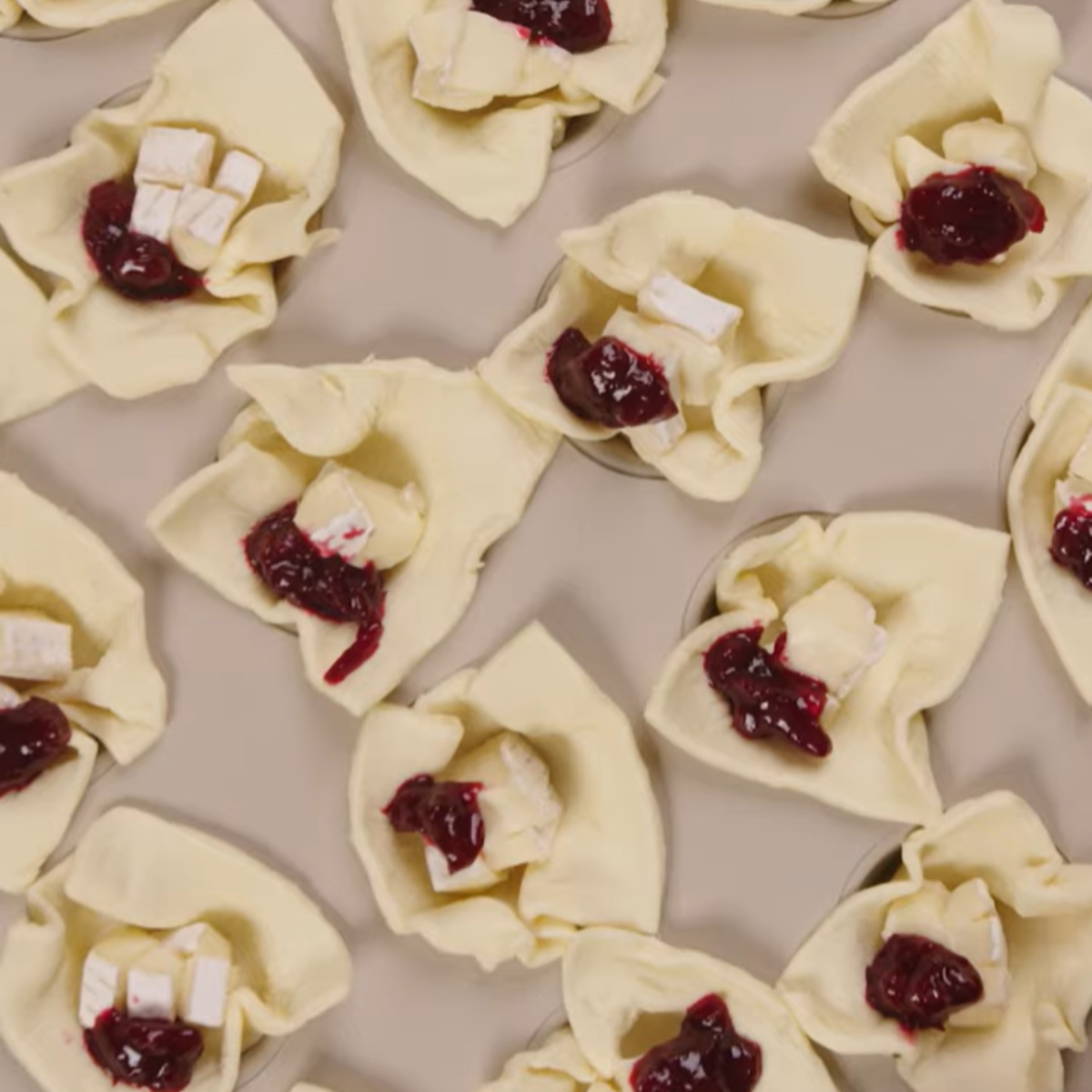 Puff pastry cups filled with brie cheese and cranberry sauce, arranged on a baking sheet.