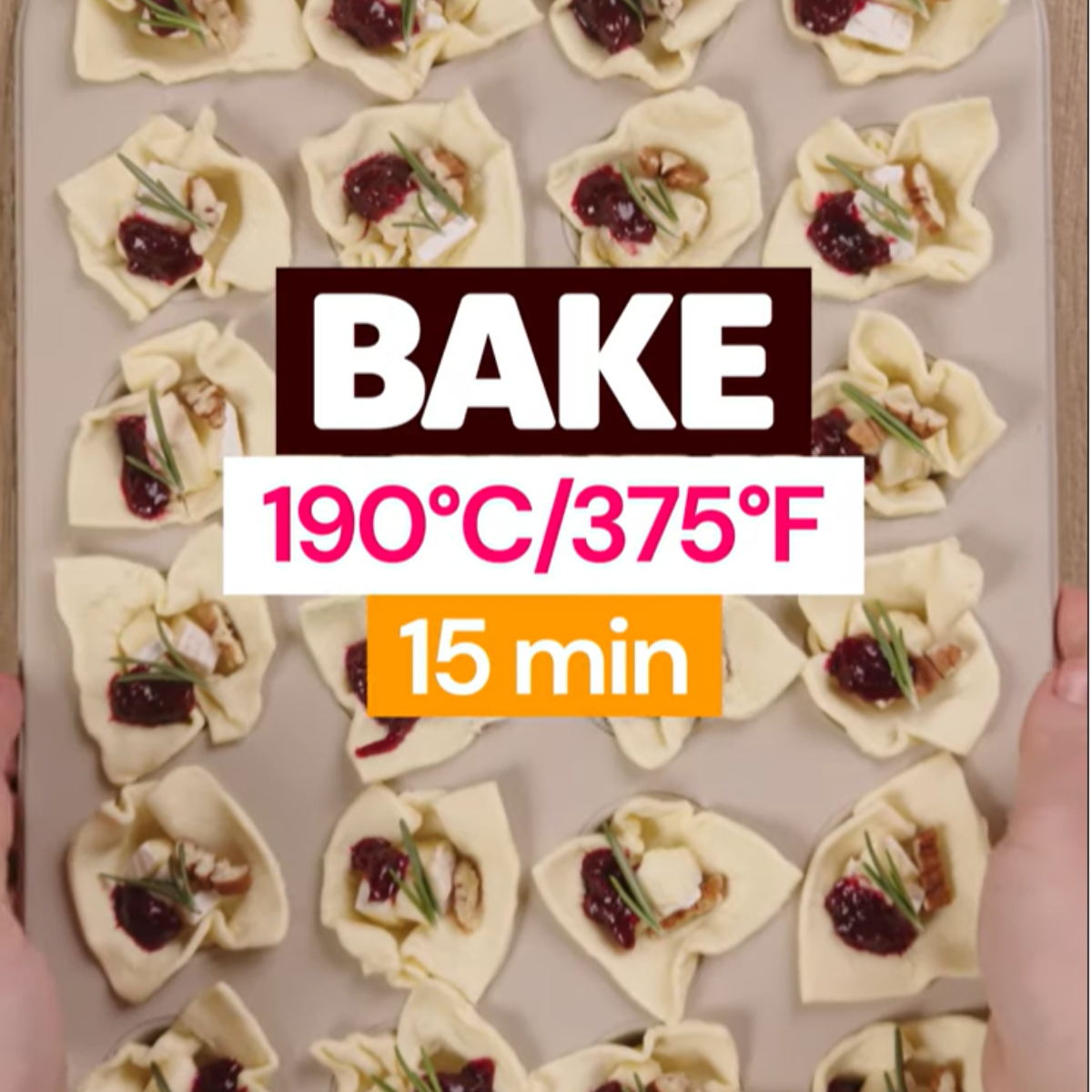A baking sheet with golden brown puff pastry cups filled with melted brie and cranberry sauce, topped with chopped pecans.