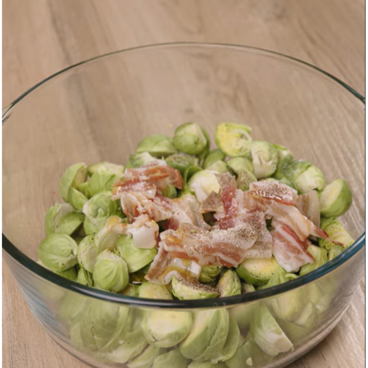 Ingredients for maple bacon Brussels sprouts: halved Brussels sprouts, bacon, and black pepper in a bowl.
